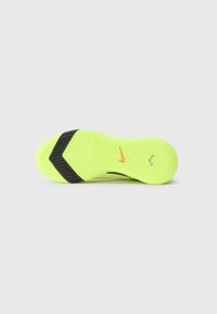 La suela de la zapatilla deportiva de color amarillo neón presenta un agarre texturizado, acentos negros y un logotipo visible en naranja cerca del centro.