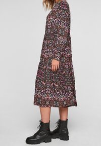 Svart blommig klänning med långa ärmar, med livfulla mönster i rosa och lila, lagerdesign och en flödande silhuett, kombinerad med svarta snörstövlar. 