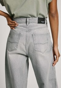 Ljust grå denimjeans med hög midja, som har bakfickor, en svart etikett och en lätt blekning i texturen.