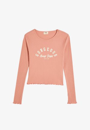 Długi rękaw, prążkowany top w jasnoróżowym kolorze z okrągłym dekoltem, z białym napisem "GORGEOUS Always Joyful" i falistym dołem.