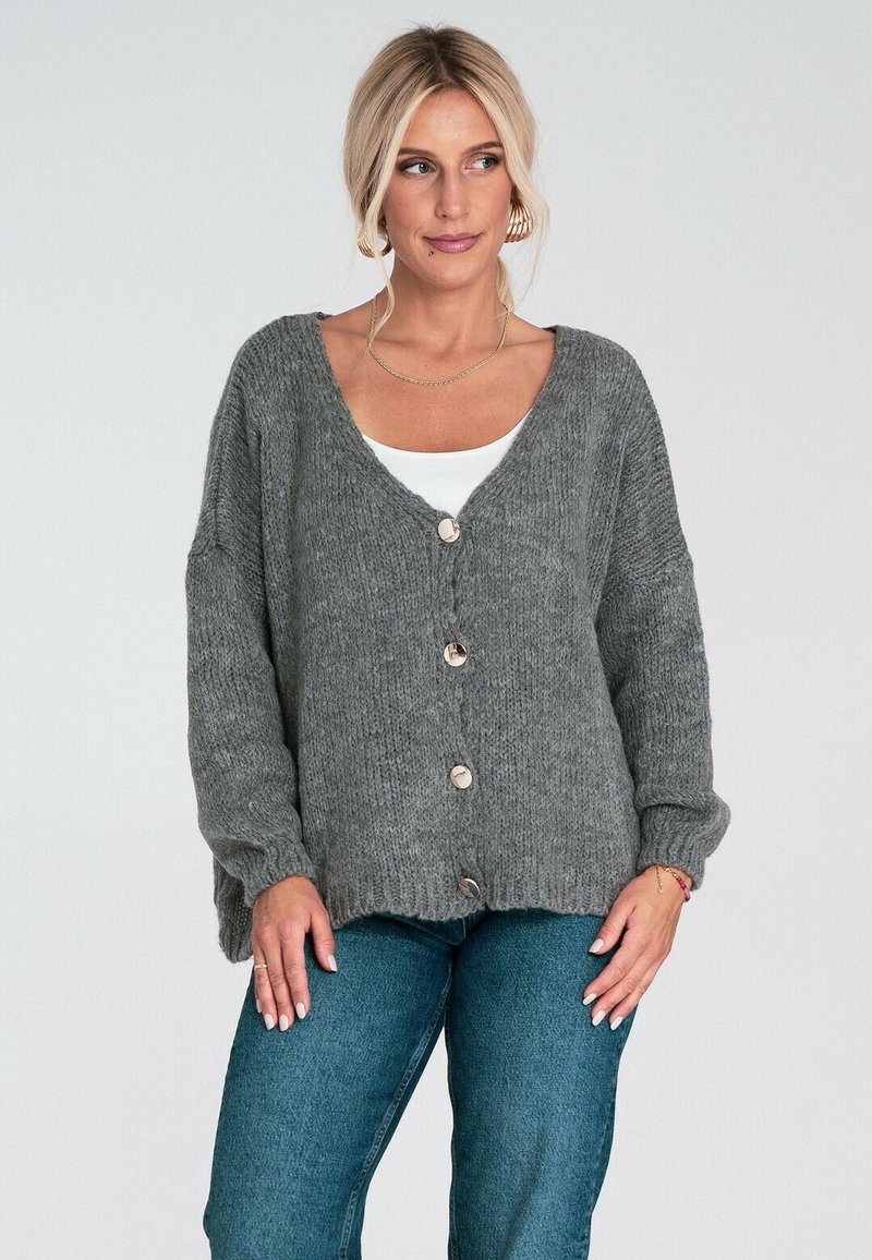 Szary dziany kardigan z dekoltem w serek, długimi rękawami i dużymi guzikami. Teksturowana tkanina o luźnym kroju, zestawiona z białą bluzką i niebieskimi dżinsami.