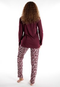 Top a maniche lunghe color bordeaux abbinato a pantaloni a fantasia floreale con disegni bianchi su uno sfondo rosso scuro; tessuto morbido con una vestibilità comoda.