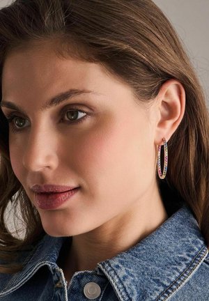 Gul hoop øreringe med farverige ædelsten, der har en glat overflade og en let struktureret tekstur, båret af en model mod en neutral baggrund.