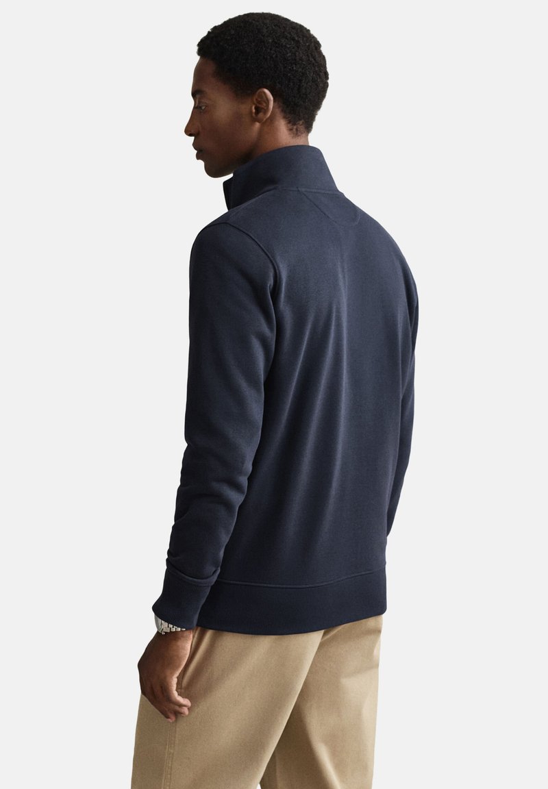 Sweat-shirt bleu marine avec col montant et manches longues, confectionné en tissu doux. Présente des coutures texturées le long des coutures et des poignets.
