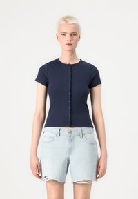 Haut à manches courtes côtelé navy avec un col rond et une fermeture par boutons à l'avant, associé à un short en denim déchiré bleu clair.