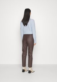 Lyseblå strikket sweater, brune bukser i faux læder, cremefarvede ankelstøvler med blokhæle. Fokus på tekstur og farvekontrast.