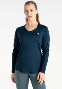 Dunkelblaues langärmliges Sportshirt mit V-Ausschnitt. Besitzt einen strukturierten Stoff und ein kleines Logo auf der Brust. Kombiniert mit grauen Leggings.