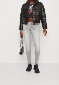 Giacca a vento nera con design corto, abbinata a jeans skinny grigio chiaro. Una borsa nera e sneakers scure completano il look.