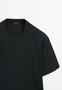Černé tričko s krátkým rukávem a kulatým výstřihem, se viditelnou etiketou Massimo Dutti uvnitř límce, položené na bílé ploše.