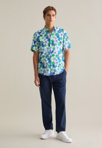 Camisa de manga corta con botones, con un patrón floral en azul, verde y blanco, combinada con pantalones marinos y zapatillas blancas.
