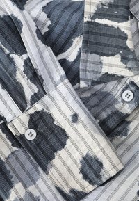 Κοντινό πλάνο μανσετών πουκάμισου με ασπρόμαυρο σχέδιο tie-dye, κουμπιά και κάθετες λεπτές μαύρες ρίγες.
