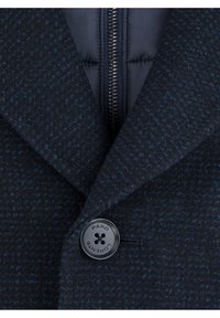 Granatowy, strukturalny płaszcz w wzór houndstooth, z czarnym guzikiem oznaczonym napisem „PAKO LORENTE” oraz centralnym zamkiem błyskawicznym.