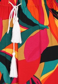 Kleurrijke stof met grote bloemenpatronen in roze, oranje, groen en zwart, met een witte trekkoord en tassel-details.