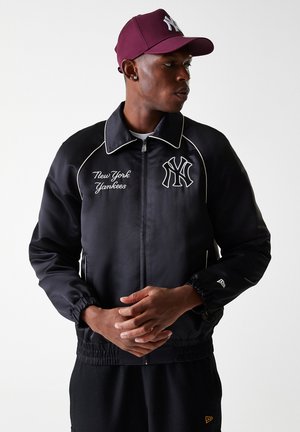 Black nylon jacket with white stitching, "New York Yankees" text, and embroidered logo; features a zip front and elastic cuffs. Burgundy cap.
