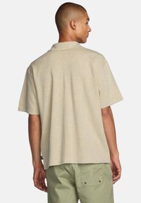 Kortærmet beige polo skjorte med subtilt bladmønster, afslappet pasform og klassisk krave. Sammen med lysegrønne bukser.