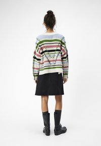 Suéter de punto multicolor con rayas horizontales en verde, rosa y azul, combinado con una falda negra y botas negras hasta la rodilla.