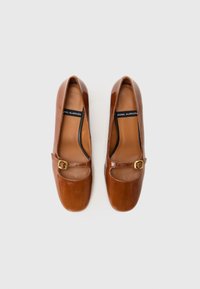 Brown leather shoes with a rounded toe, featuring a small cut-out and strap with a gold buckle accent. Smooth texture throughout.