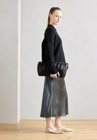 Pull en maille noir, jupe midi en satin argenté, pochette plissée noire et escarpins beiges à bout pointu avec des accents décoratifs.