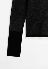 Manche longue noire avec un poignet noir uni et un tissu foncé transparent au-dessus, sur fond blanc.