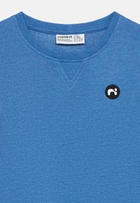 Modrá bavlnená mikina s okrúhlym výstrihom, rebrovanými manžetami a malým čiernym kruhovým logom na prednej strane. Mäkká textúra s melírovaným vzorom.