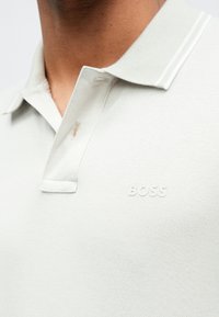 Jasnoszara koszulka polo wykonana z teksturowanej tkaniny, z dwukolorową plisą zapinaną na guziki i subtelnym logo "BOSS" na piersi.