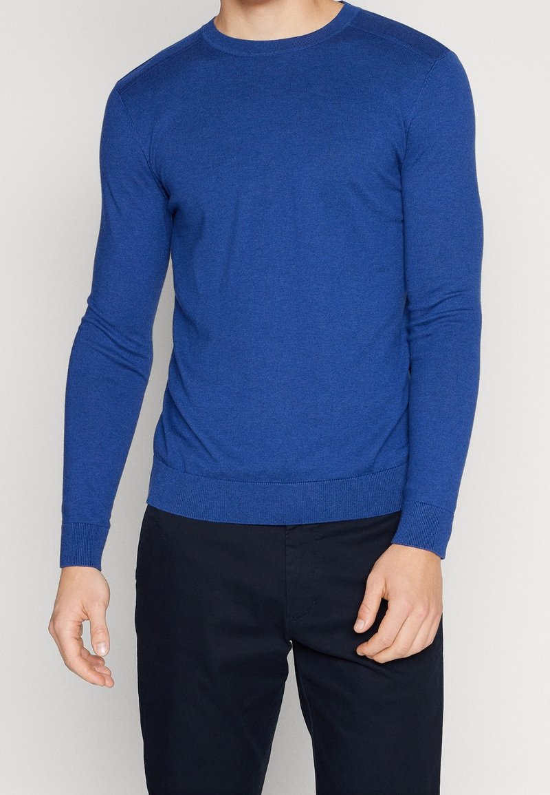 Suéter azul de cuello redondo hecho de una suave tela de punto. Mangas largas, puños ajustados y un dobladillo recto. Textura suave con un color sólido. Sin patrones.