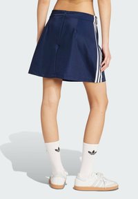 Mornarska suknja s nabranim stranama i tri bijele pruge. Nosio se s bijelim tenisicama i bijelim čarapama do koljena s crnim logom.