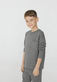 Šedá mikina s dlouhým rukávem, kulatým výstřihem a přední kapsou, v kombinaci se sladěnými šedými kalhotami, s jemnou texturou a volným střihem.