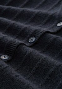 Marineblaue Strickjacke aus weicher Wolle, mit horizontaler Rippstruktur und runden blauen Knöpfen entlang der Vorderseite.