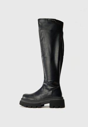 Black knee-high boots made from smooth leather, featuring a chunky rubber sole and a logo patch on the top. Sleek design with minimal accents.