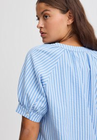 Blusa a righe blu con una vestibilità rilassata, scollo rotondo, dettaglio plissettato sul retro e maniche corte arrotolate con bottoni.