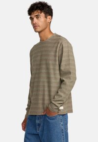 Langärmliges Shirt mit Rundhalsausschnitt in olivgrün, mit dezenten horizontalen Streifen und einer strukturierten Oberfläche. Das Etikett ist in der Nähe des Saums sichtbar.