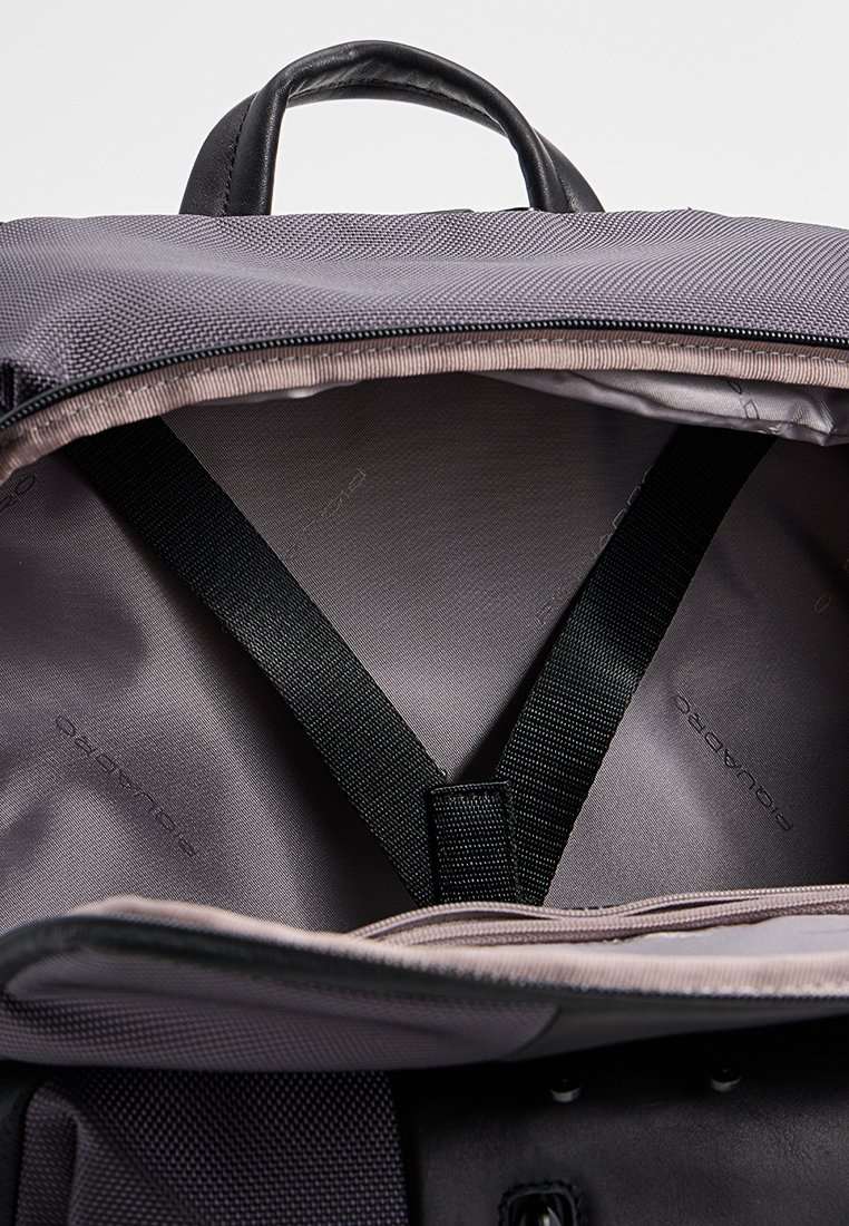 Interno del zaino discreto in tessuto grigio, con strap nere e una fodera liscia. Progettato per un'organizzazione leggera e facile durante i viaggi.