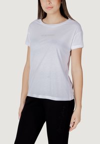 T-shirt bianca in cotone con maniche corte, scollo rotondo, con "Armani Exchange" ricamato al centro, indossata con pantaloni neri.