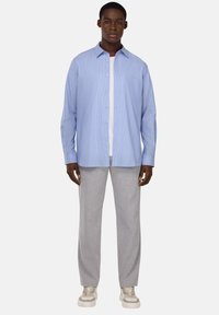 Camicia azzurro chiaro con colletto e un leggero motivo a righe, abbinata a pantaloni grigi a gamba dritta e sneakers beige. Maglietta bianca visibile.