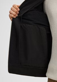 Zwarte zip-jack binnenkant met een gladde stof voering, ruime zak en een gestructureerd materiaal op het bovenste gedeelte.