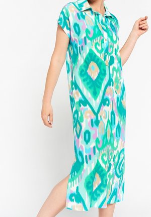 Femme portant une robe boutonnée à manches courtes et longueur genou avec un motif abstrait bleu sarcelle, turquoise, beige et lavande.