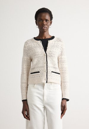 Beige gebreide cardigan met geometrische patronen, zwarte zoom langs de randen en twee zwarte zakken. Knopen aan de voorkant.