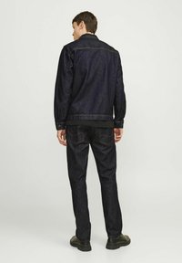 Chaqueta y pantalones de mezclilla azul oscuro, con un diseño clásico, costuras visibles y un corte ajustado. Unos zapatos negros completan el conjunto.