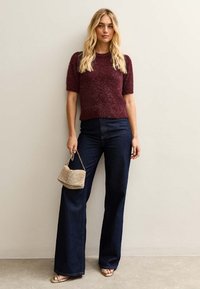 Burgundowy sweter z krótkim rękawem o miękkiej teksturze, w połączeniu z szerokimi ciemnoniebieskimi dżinsami. Uzupełniony małą beżową plecioną torebką.