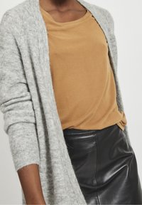 Lys grå strikket cardigan med lange ærmer, parret med en sennepsgul t-shirt og en sort læderskirt. Blød tekstur og afslappet pasform.