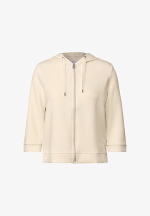 Chaqueta con capucha de color crema, con cremallera completa, hecha de una tela suave, que presenta un ajuste relajado, mangas largas y cordones decorativos en la capucha.