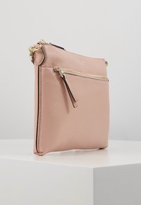 Růžová kožená kabelka přes rameno s hladkou strukturou, vybavená přední kapsou na zip, zlatými kovovými doplňky a jemným logem v horní části.