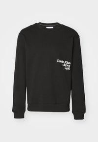 Sweat-shirt en coton noir à manches longues avec poignets côtelés. Présente un texte blanc : "Calvin Klein Jeans" et "1978" sur la poitrine.