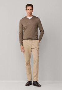 Bruine gebreide v-hals trui over een wit t-shirt, beige chinos en donkerbruine schoenen; gladde textuur en een aansluitend ontwerp.