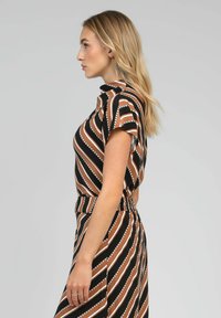 Robe rayée noire et marron avec des manches courtes, une taille cintrée et une silhouette fluide. Les motifs incluent des accents à pois blancs.