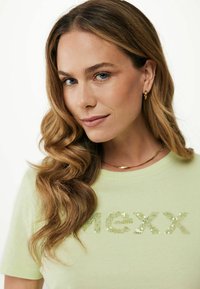 Světle zelené bavlněné tričko s vyšívaným nápisem "MEXX". Měkká struktura, krátké rukávy, kulatý výstřih, s volným střihem.