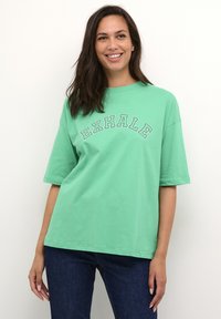 Groene katoenen t-shirt met korte mouwen, met een "EXHALE" grafiek in witte omlijnde letters over de borst. Eenvoudige, relaxte pasvorm.