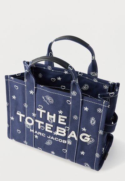 Granatowa torba płócienna z białymi wzorami florystycznymi i gwiazdkami, z dwoma uchwytami oraz haftem "THE TOTE BAG MARC JACOBS" z przodu.