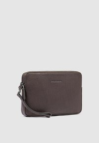 Borsetta in pelle marrone con chiusura a zip, cinturino da polso e marchio discreto sulla parte anteriore. Presenta una texture liscia e una forma rettangolare.